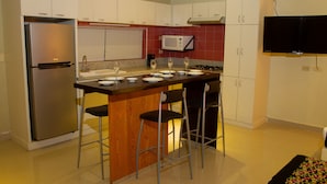 A modern kitchen with a stainless steel refrigerator, a microwave, a sink, and a bar area with stools.