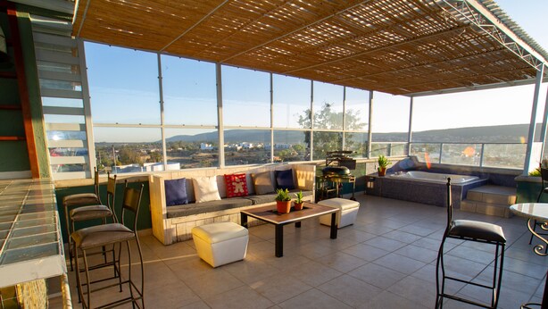A spacious outdoor seating area with a view of the cityscape, a wooden pergola, and a bar area with stools.
