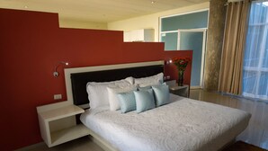 A modern bedroom with a large bed, white bedding, and a red accent wall.