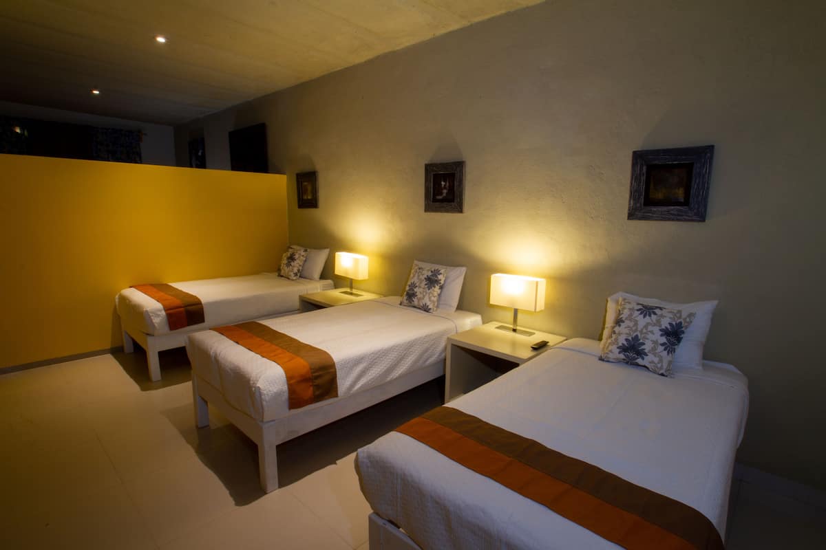 A hotel room with three single beds, each with a bedside table and lamp.