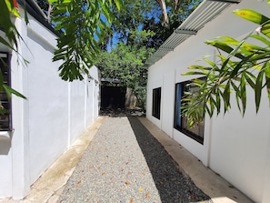 A narrow pathway with gravel, flanked by white walls and large windows. - Casa BRUJA (Cahuita)