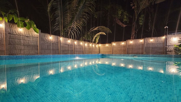 A nighttime swimming pool with clear blue water, surrounded by stone walls and palm trees. - Casa BRUJA (Cahuita)