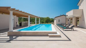 Une piscine rectangulaire, agrémentée d’une pergola et de chaises longues d’un côté, et d’un mur en pierre de l’autre.