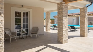 Un espace extérieur abrité, doté de piliers en pierre, d’une piscine, de chaises longues et d’une table avec des chaises.