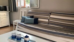 Un canapé à rayures avec des coussins, une petite table blanche avec deux tasses et une théière, et une fenêtre avec des rideaux.