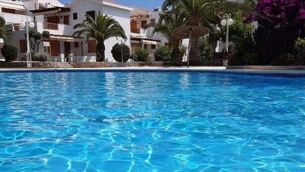Une piscine d’un bleu éclatant, entourée de bâtiments blancs dotés de balcons et de palmiers.