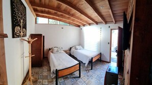 A room with two single beds, a wooden ceiling, a coat rack, a television, and a patterned floor.