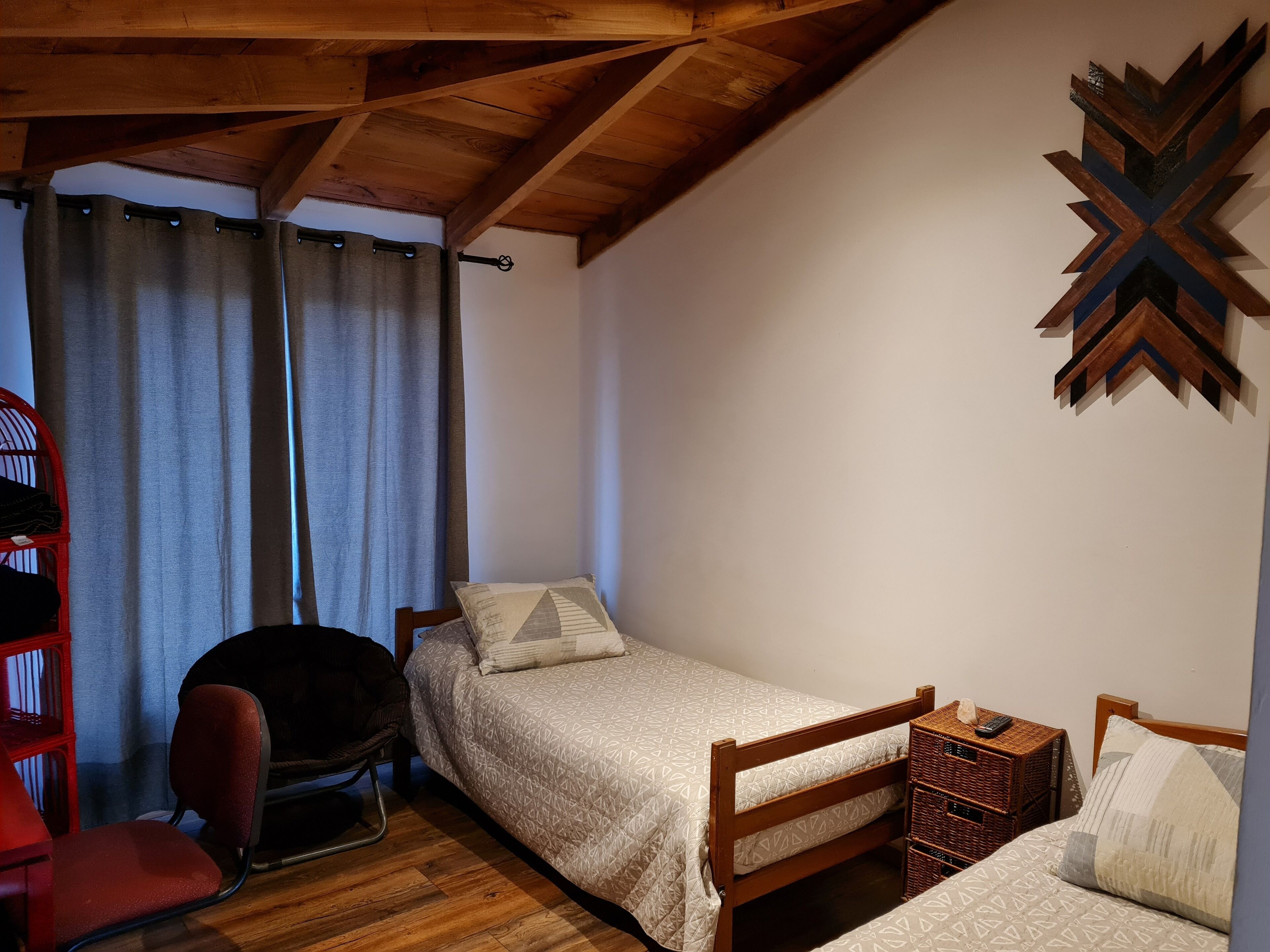 A small, cozy bedroom with a wooden ceiling, a single bed, a chair, and a red chair.