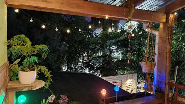 A cozy outdoor seating area with string lights, potted plants, and a wooden bench.