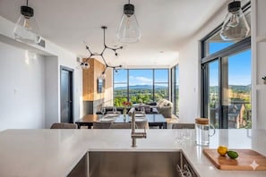 A modern kitchen with a large island, dining area, and a view of the countryside. - 3BR Tremblant Condo | Lake-Mtn Views & Hot Tub (Mont-Tremblant)