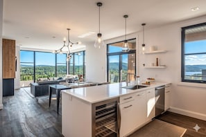 A modern kitchen with a central island, large windows, and a dining area with a view. - 3BR Tremblant Condo | Lake-Mtn Views & Hot Tub (Mont-Tremblant)