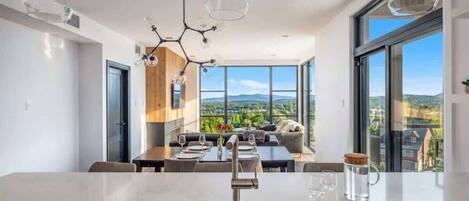 A modern kitchen with a central island, large windows, and a dining area with a view.