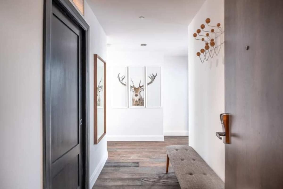 A hallway with a wooden floor, a bench, framed deer artwork, and a door with a modern handle.