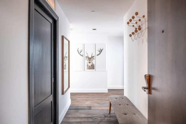 A hallway with a wooden floor, a bench, framed deer artwork, and a door with a modern handle.