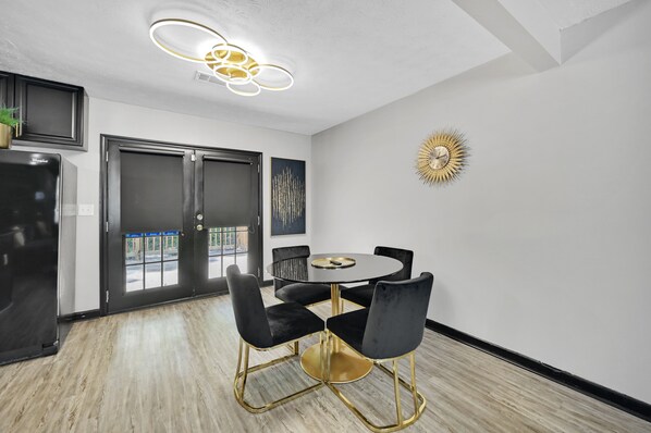 Una cocina moderna con un refrigerador negro, una mesa de comedor con cuatro sillas negras y un adorno decorativo en forma de sol en la pared.