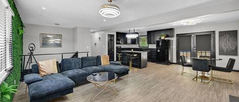 Una sala moderna con un sofá modular, una mesa de centro de cristal y un comedor con una mesa redonda y sillas.