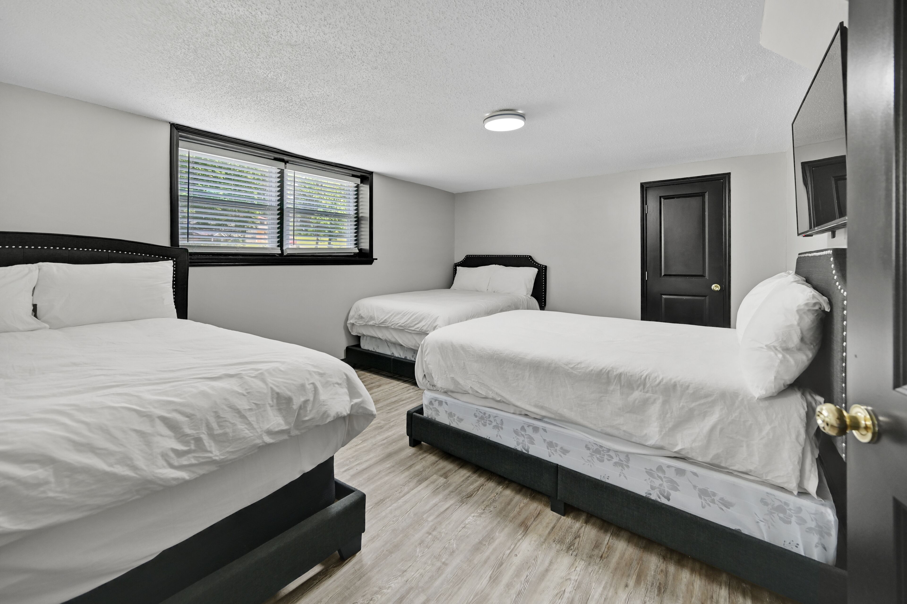 Un dormitorio con dos camas individuales, una ventana con persianas, una puerta y un espejo en la pared.