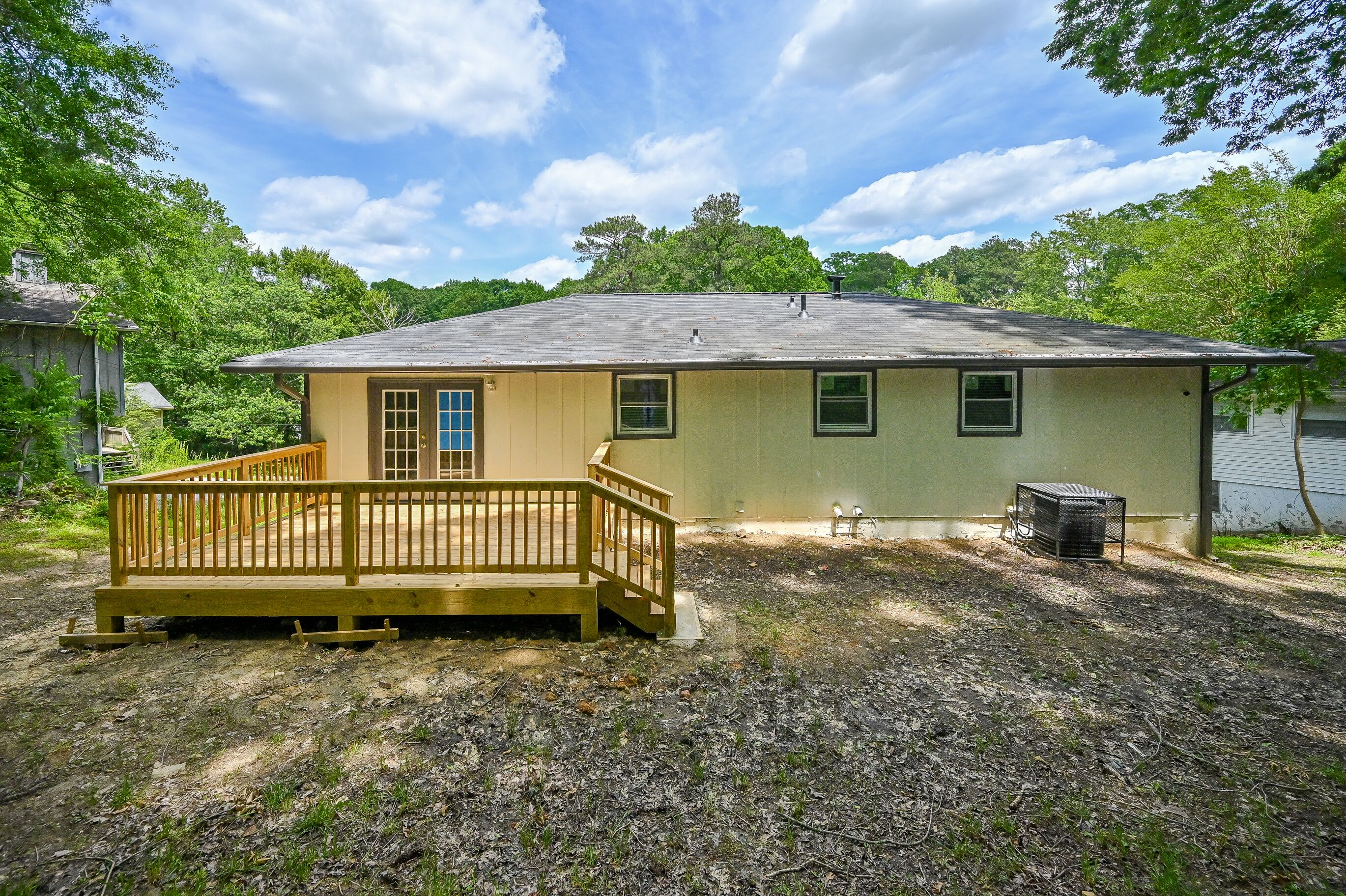 A single-story house with a wooden deck, a small attached garage, and a yard with trees.