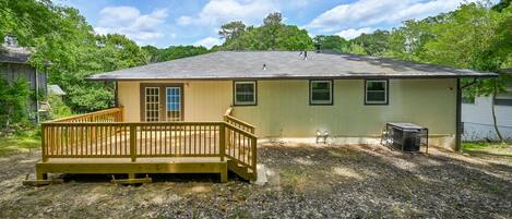 A single-story house with a wooden deck, a small attached garage, and a yard with trees.