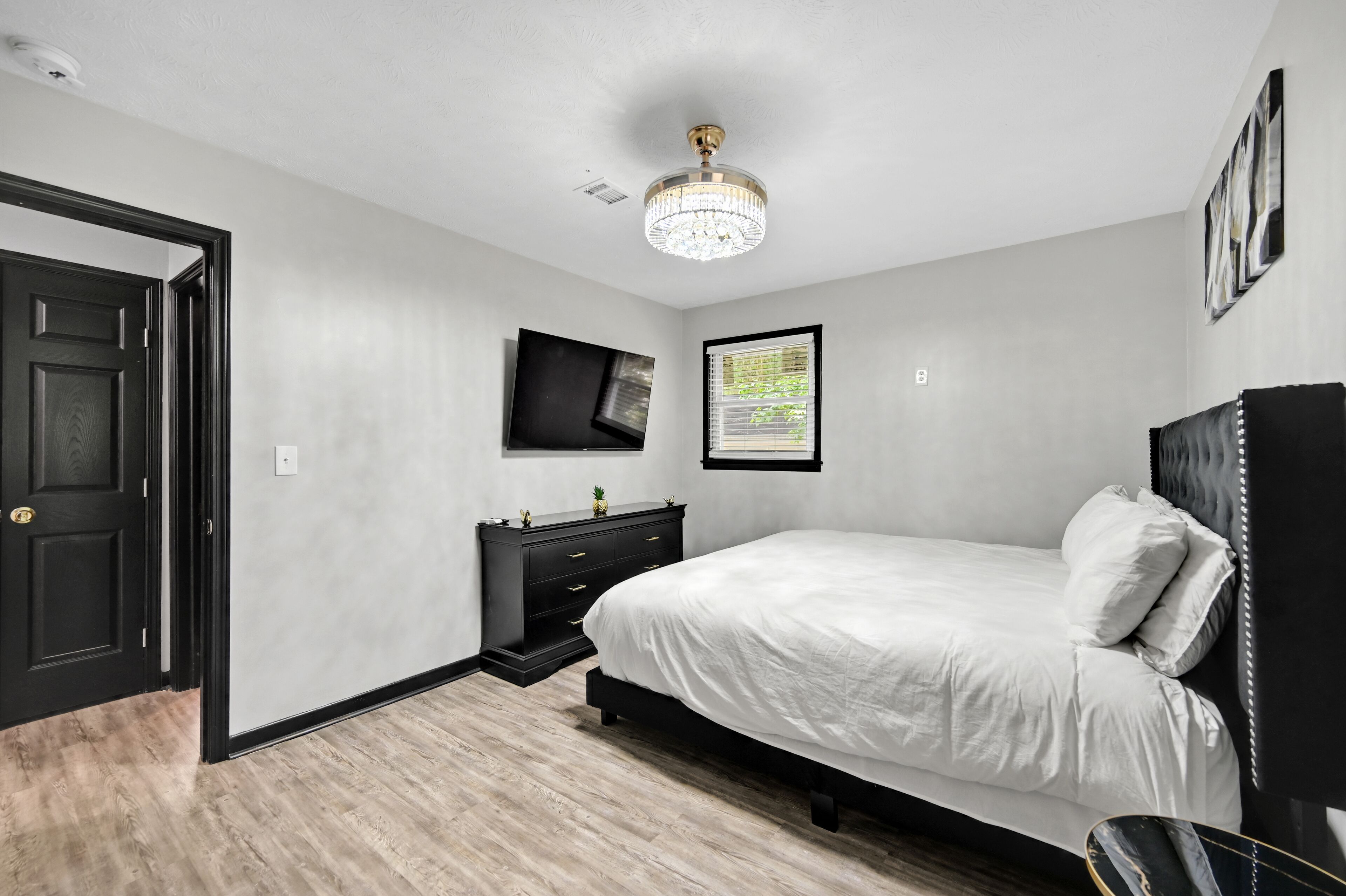 A bedroom with a bed, a dresser, a television, and a chandelier.
