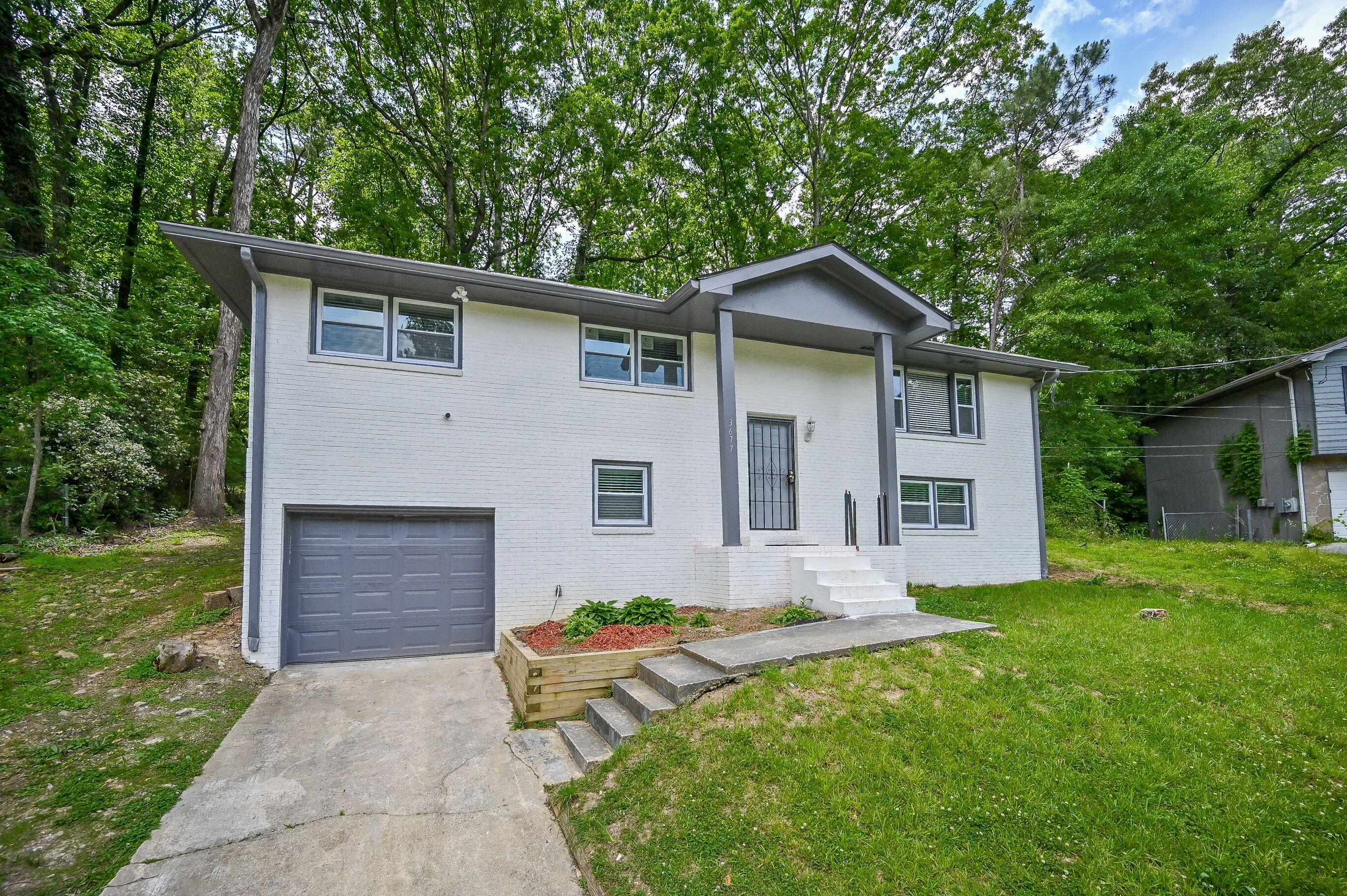 A two-story house with a garage, a front porch, and a small front yard with a wooden planter.