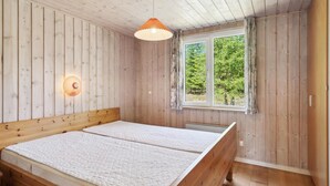 A room with wooden walls and ceiling, a bed with a white quilt, a window with a view of trees, and a hanging light fixture.