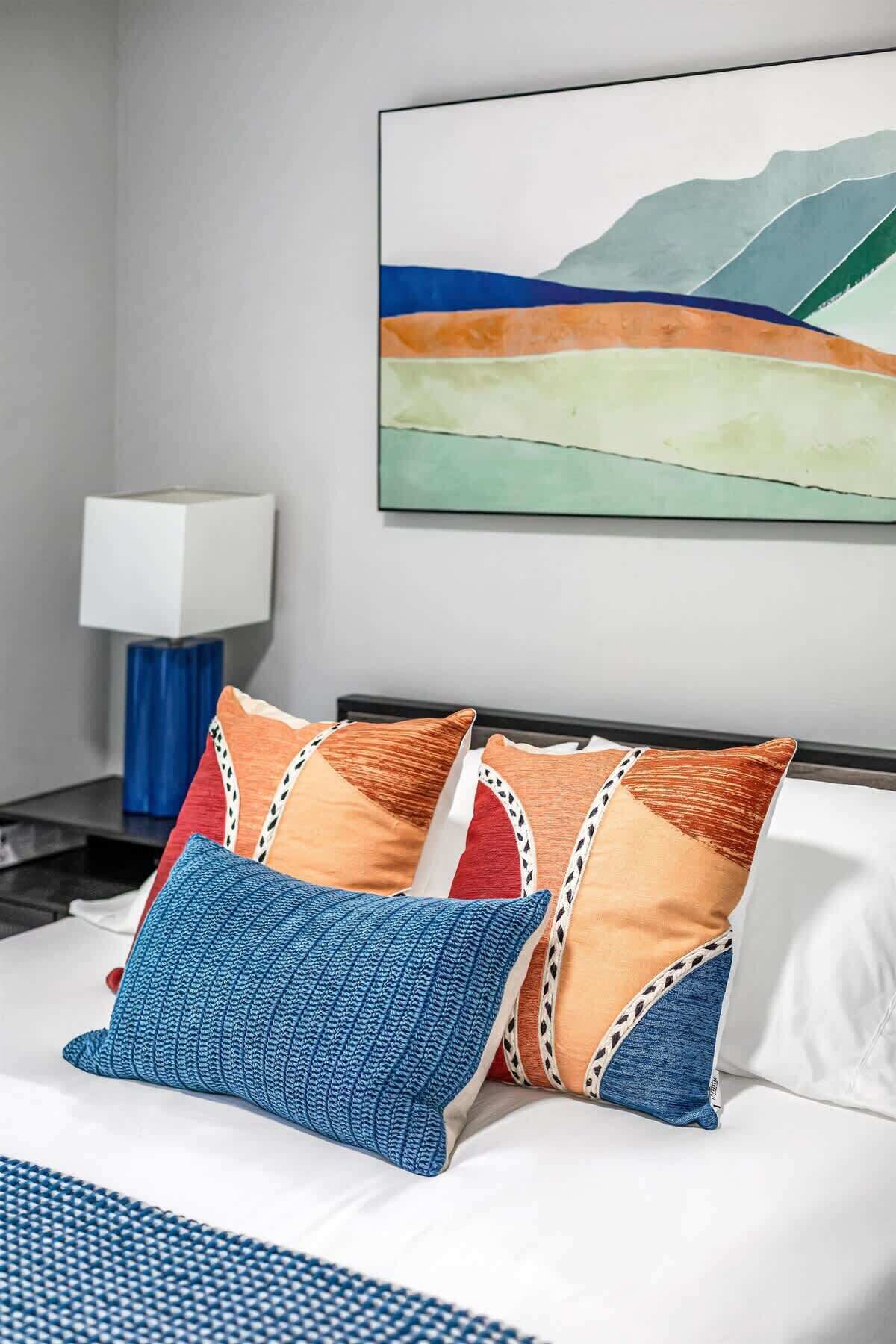 Une chambre d’hôtel avec un lit, des oreillers, une table de chevet, une lampe et un tableau au mur.