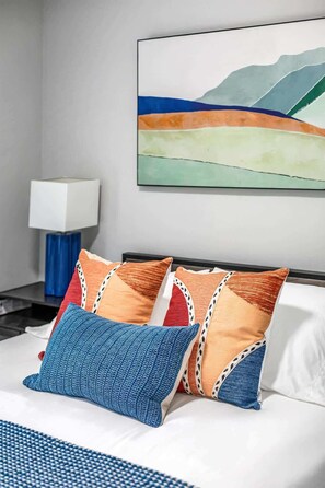 A hotel room with a bed, pillows, a nightstand, a lamp, and a painting on the wall. - 5BR - 12 Mins to Downtown 6 Queens + Free Parking (Detroit)