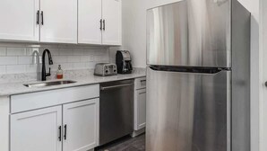 A modern kitchen with white cabinets, a stainless steel refrigerator, a coffee maker, and a toaster. - 5BR - 12 Mins to Downtown 6 Queens + Free Parking (Detroit)