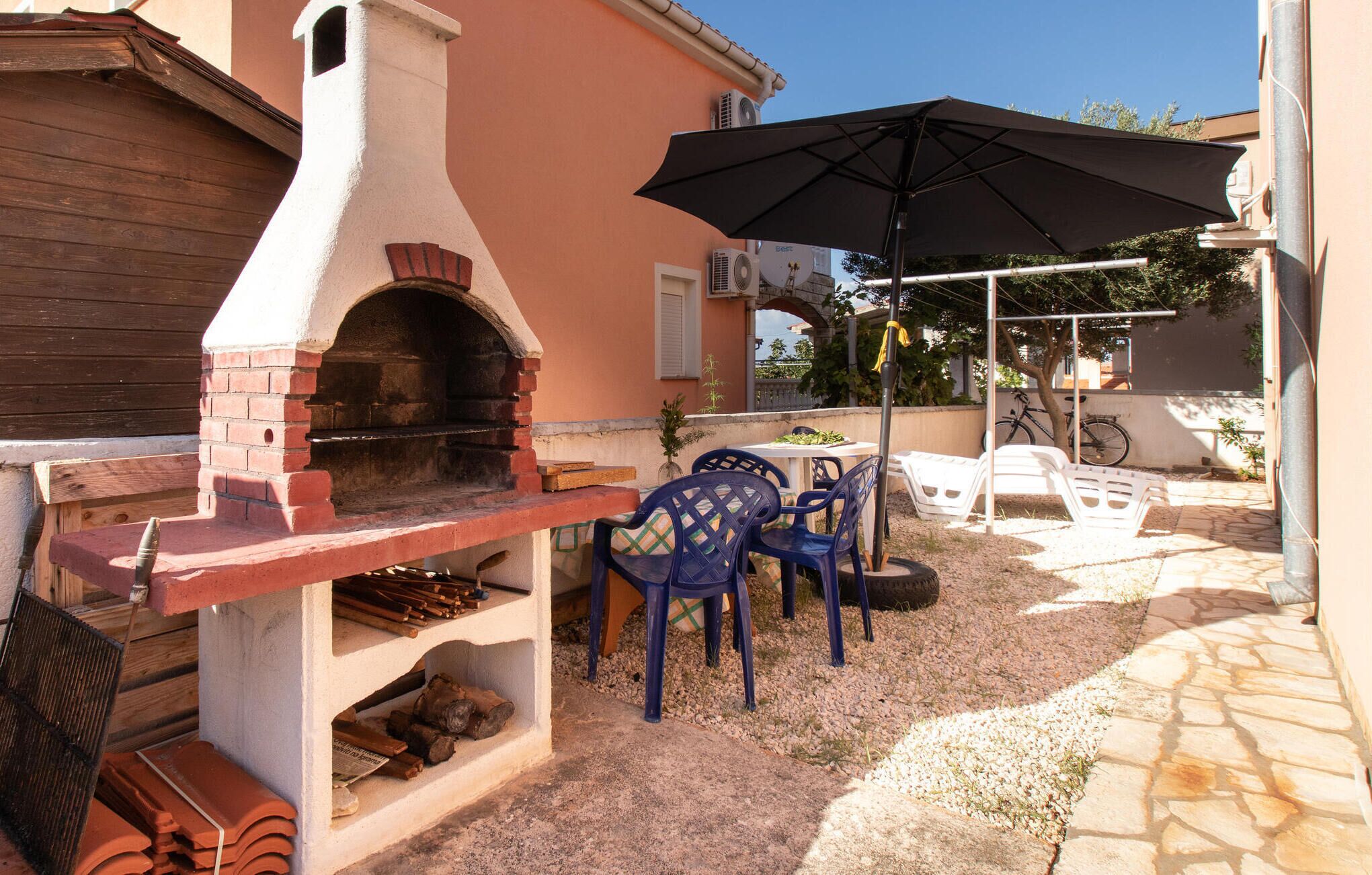 Eine Terrasse im Freien mit einem Backofen aus Ziegeln, Plastikstühlen und einem Sonnenschirm.
