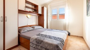 A bedroom with a bed, a wooden wardrobe, a shelf with decorative items, a wall-mounted light, and a window with a view of the outside. - Amazing apartment in Vir with WiFi (Vir)