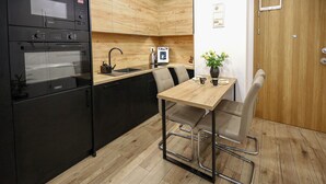 Eine kompakte Küche mit integriertem Ofen, Spüle und Kaffeemaschine. Ein Tisch mit zwei Stühlen und eine Vase mit Blumen sind ebenfalls vorhanden.
