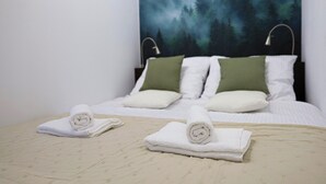 Ein ordentlich bezogenes Bett mit zwei aufgerollten Handtüchern, einem Wandbild mit Waldmotiv und einem schlichten, klaren Raumdesign.