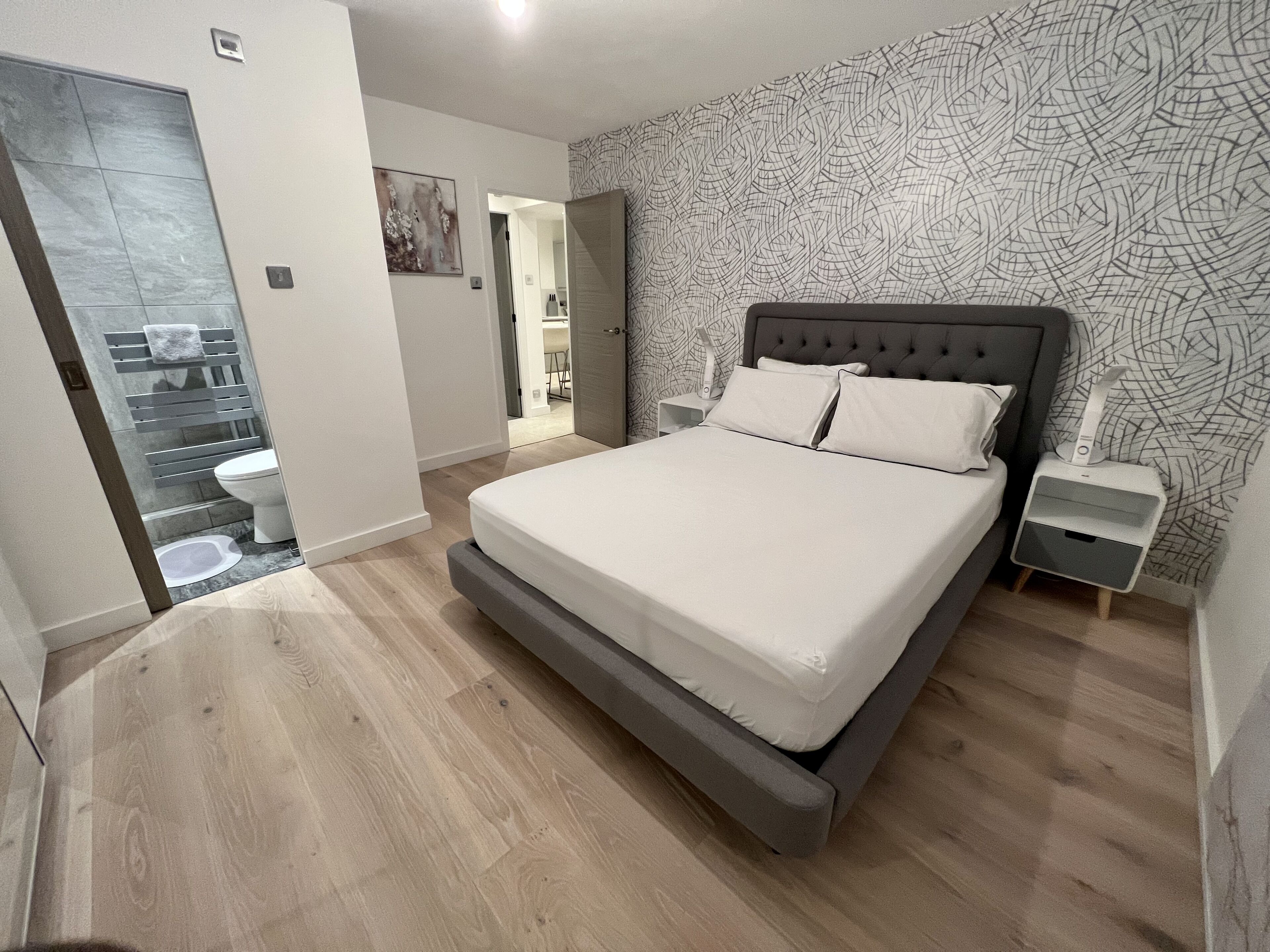 Ein Schlafzimmer mit einem großen Bett, einem Nachttisch, einem Badezimmer mit Toilette und Dusche sowie einem Flur, der in einen weiteren Raum führt.