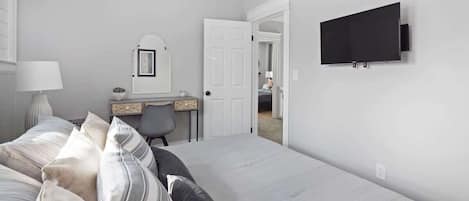 Une chambre à coucher comprenant un lit, un bureau, une chaise, un téléviseur et une porte donnant sur une autre pièce.