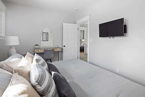 A bedroom with a bed, a desk, a chair, a television, and a door leading to another room.