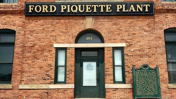 A brick building with a sign reading 'FORD PIQUETTE PLANT' and a plaque with historical information.