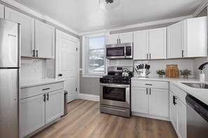 Une cuisine moderne avec des meubles blancs, des appareils électroménagers en acier inoxydable et un plancher en bois.
