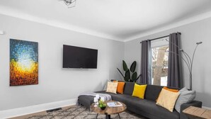 A modern living room with a sofa, a coffee table, a flat-screen TV, and a large abstract painting.