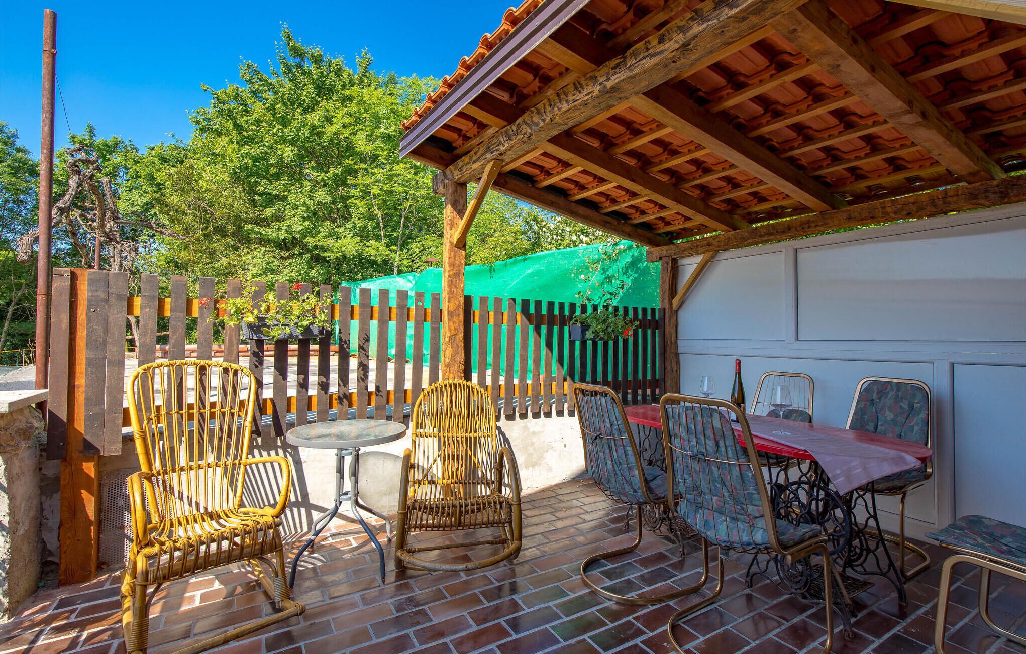 An outdoor patio with wicker chairs and a table, surrounded by a wooden fence and a green tarp.