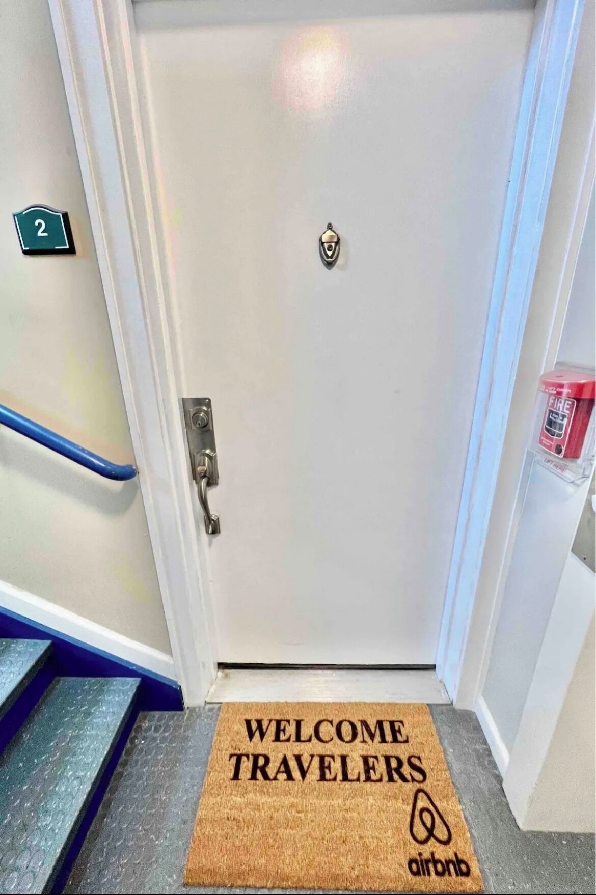 A door with a doormat that reads "WELCOME TRAVELERS" and the Airbnb logo.