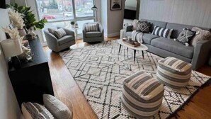 Uma sala de estar moderna com um sofá cinza, pufes listrados e um tapete estampado.