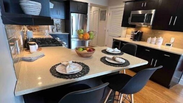 Uma cozinha moderna com ilha central, cadeiras pretas e micro-ondas.