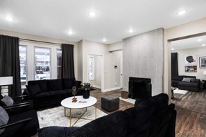 Ein modernes Wohnzimmer mit Kamin, schwarzen Sofas und einem weißen Couchtisch.