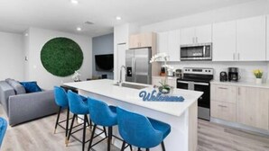 A modern kitchen with white cabinets, a central island with blue bar stools, and a green circular accent wall.