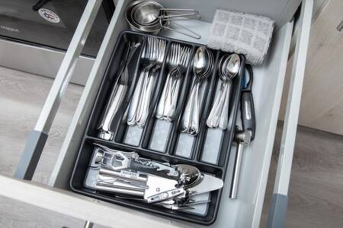 A drawer containing a set of silverware, including forks, knives, and spoons, neatly arranged in compartments.