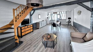 Ein geräumiger Wohnbereich mit einer Holztreppe, einem Esstisch mit Stühlen, einer Couch und einem Couchtisch.