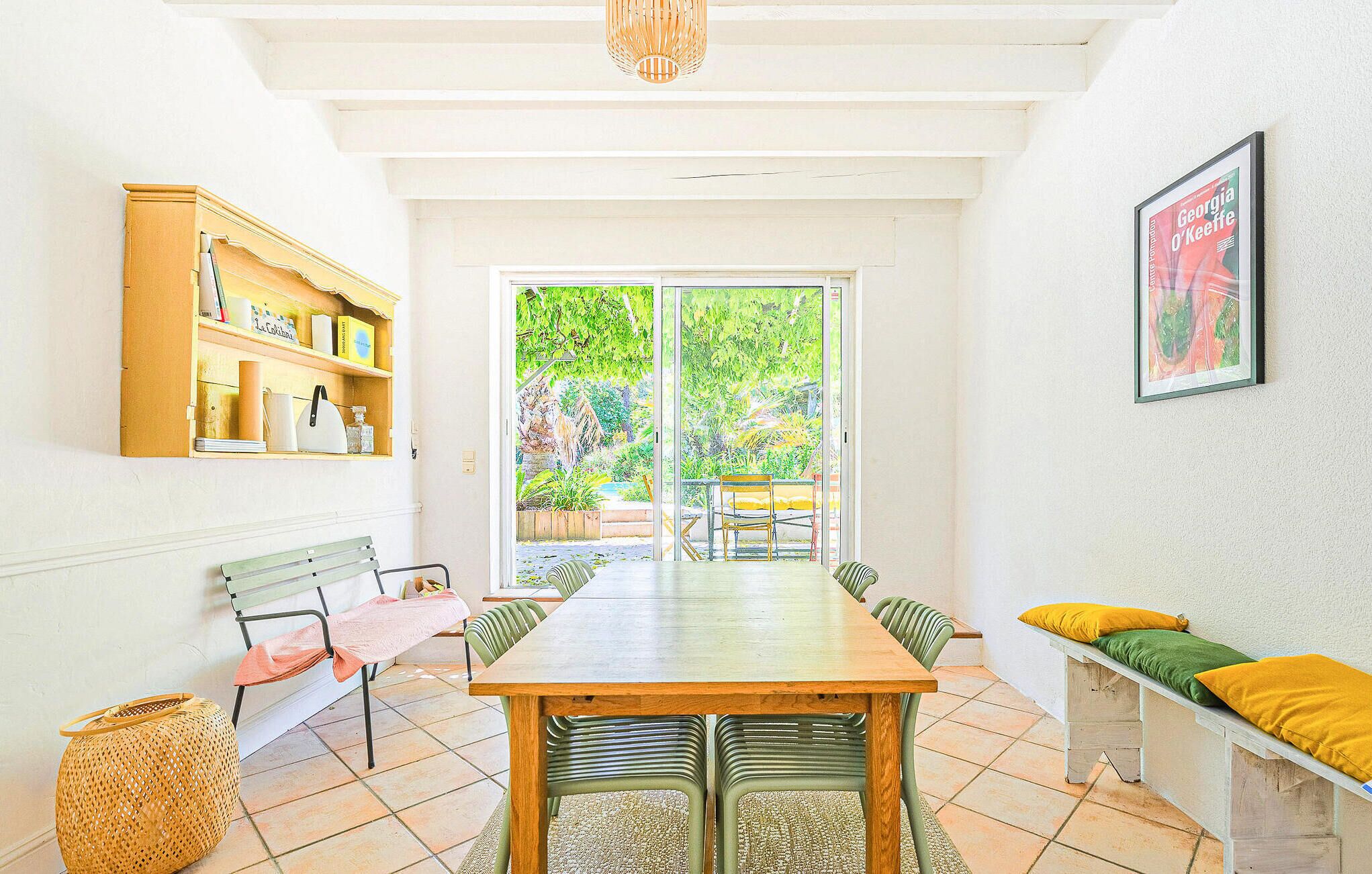 Un coin repas avec une table et des chaises en bois, un banc avec des coussins, une bibliothèque et un tableau encadré au mur.