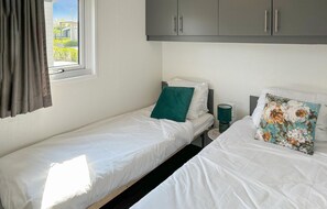 Une chambre avec deux lits simples, des armoires grises au-dessus, une fenêtre avec des rideaux et une vue sur la verdure à l’extérieur.