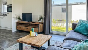 A modern living room with a sofa, a wooden coffee table, and a TV on a wooden stand. - Vakantiepark de Zeeuwse Parel (Scherpenisse)